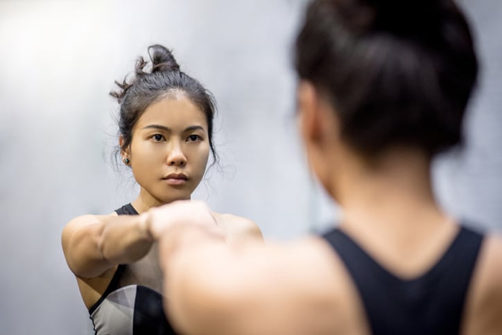young asian athletic women in sportswear punching and looking herself in the mirror